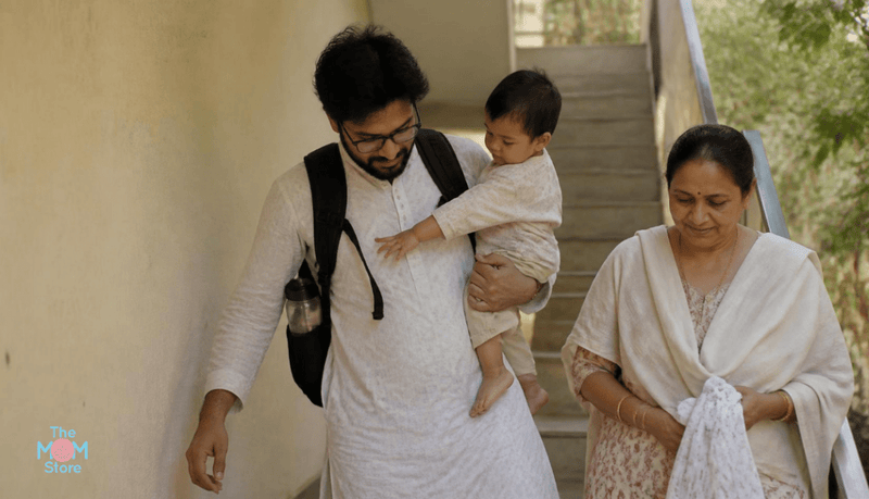Indian father carrying a black diaper backpack and his baby down apartment steps, with grandmother beside him