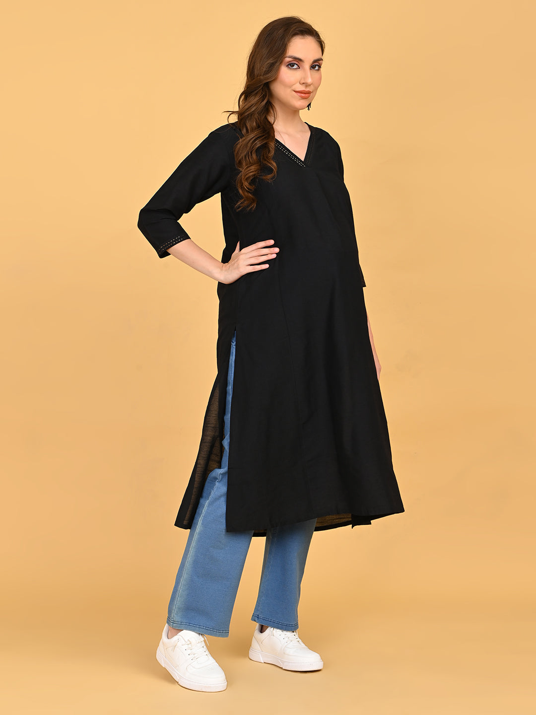 Pregnant model posing in black maternity kurta styled with blue pants and white sneakers.