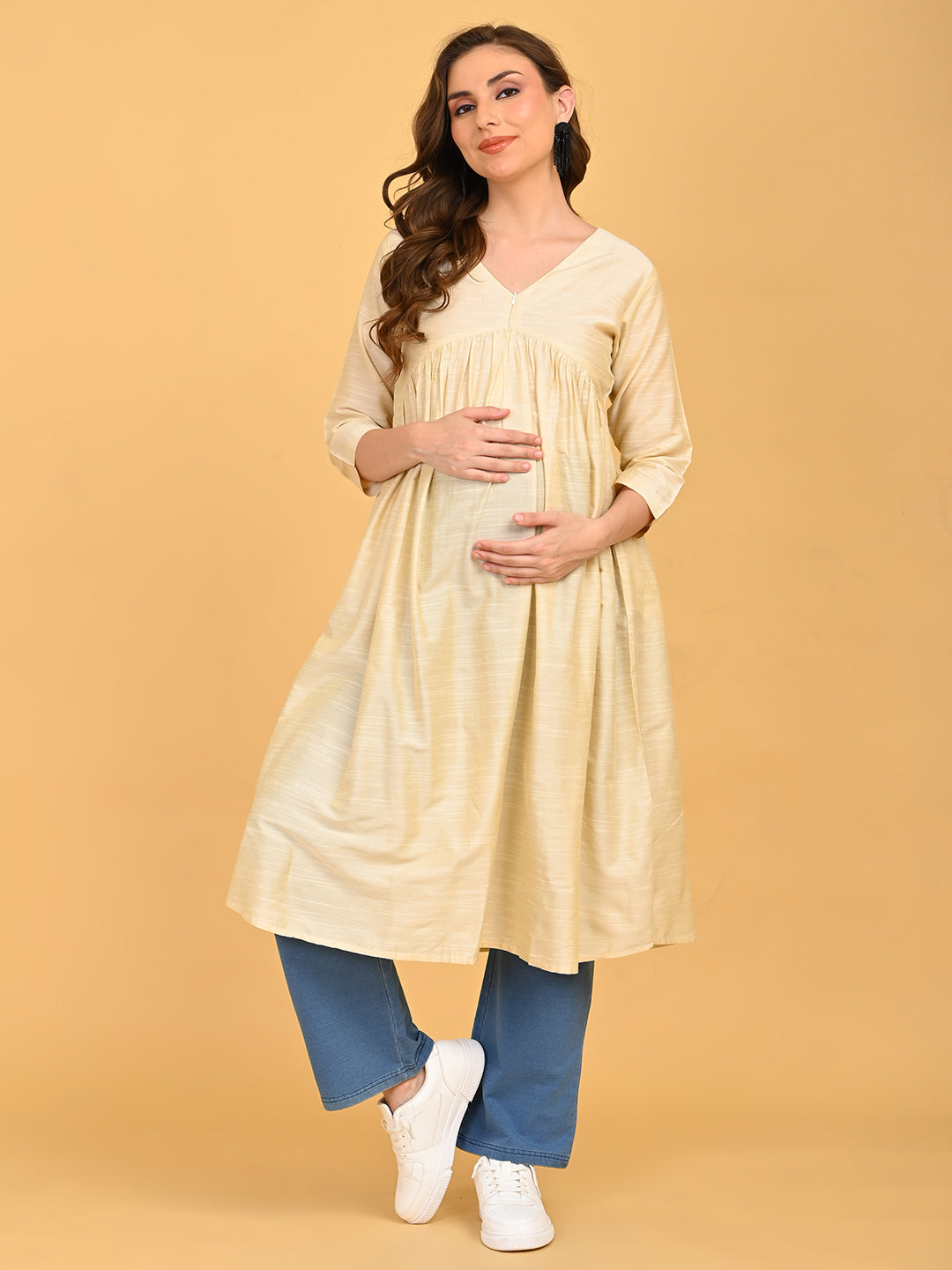 Pregnant model wearing cream silk maternity and nursing kurta with V-neckline, paired with blue straight-fit pants and white sneakers.