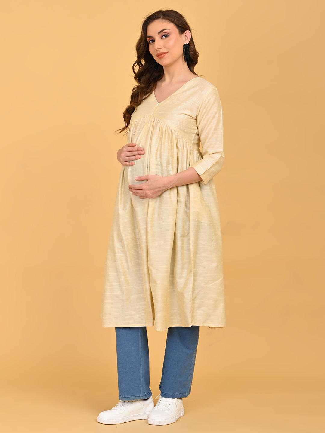 Pregnant model gently holding baby bump in cream maternity silk kurta with gathered waist detail.