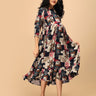 Woman twirling in The Mom Store Muted Muse maternity dress featuring vibrant patch-print design.