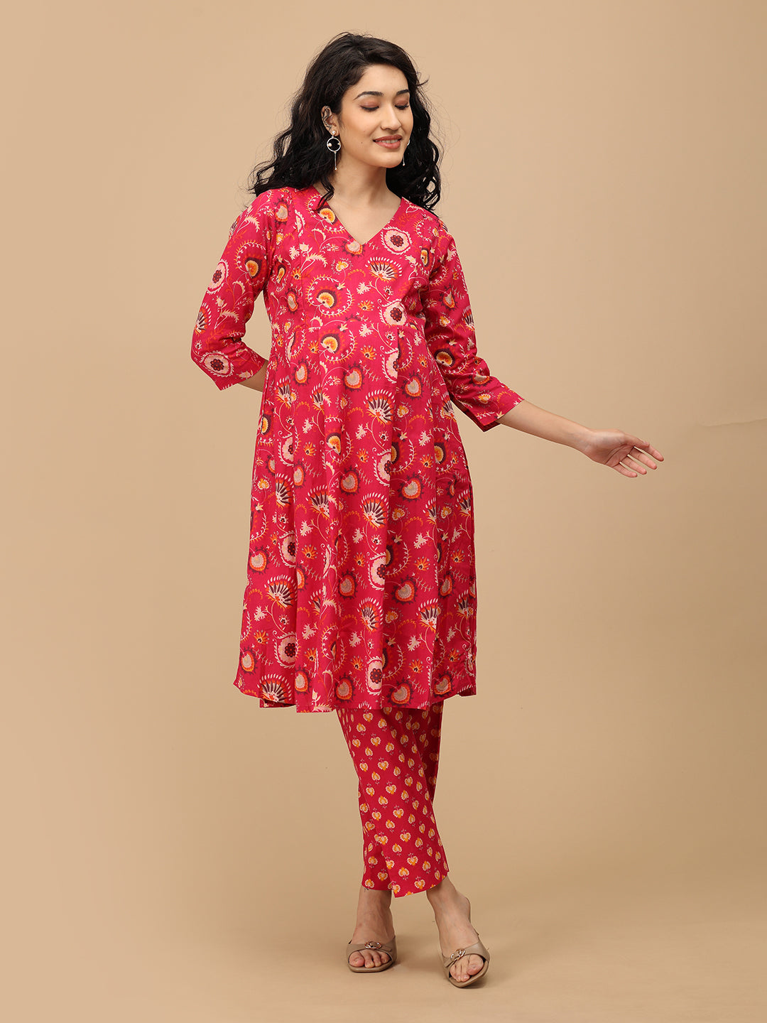 Pregnant woman wearing a bright pink printed maternity kurta with three-quarter sleeves and matching straight pants, gently holding her bump.