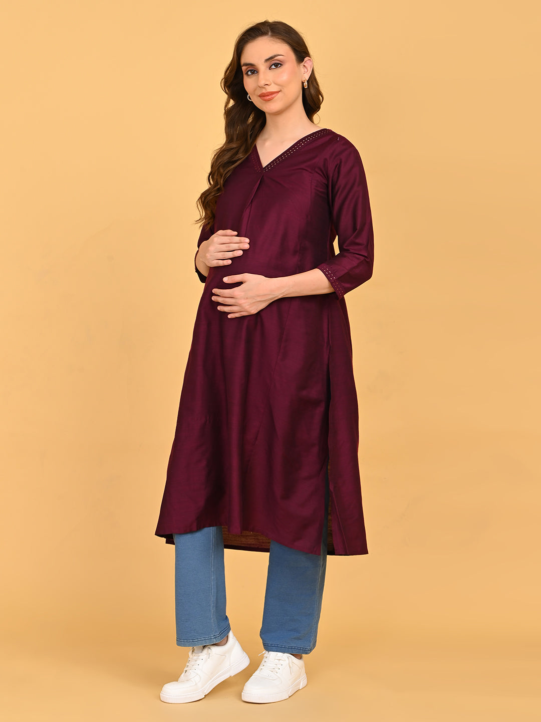 Pregnant model wearing wine maternity and nursing silk kurta paired with blue straight-fit pants and white sneakers.