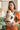 Woman using Almitra Tattva ergonomic linen baby carrier in rust and natural tones, newborn baby secured in front carry position, adjustable straps, inclusive babywearing design, breathable fabric