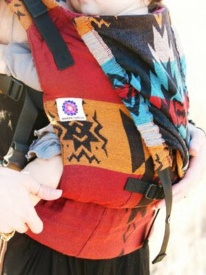 Close-up of Almitra Tattva soft structured baby carrier with vibrant Kullu-inspired geometric woven pattern, adjustable safety straps, ergonomic seating support, breathable artisan fabric, and inclusive babywearing design for infants and caregivers.