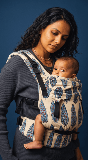 Front-side view of an infant resting securely in the Almitra Tattva Ajrakh baby carrier, highlighting the ergonomic inward-facing position and the wide, patterned waistbelt.