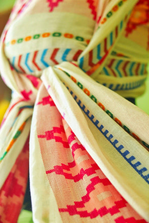 Close up of Almitra Tattva Shubra woven baby wrap featuring vibrant pink geometric motifs and multicolor bohemian stripe patterns on soft breathable fabric.