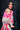 Mother carrying baby in Almitra Tattva Shubra woven baby wrap featuring bright pink geometric motifs and multicolor bohemian woven borders outdoors.