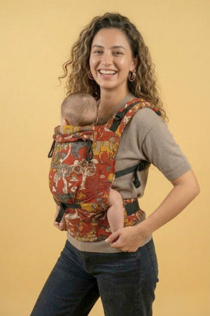 Happy caregiver wearing the Almitra Tattva Jataka Tales front-carry baby carrier with colorful traditional Indian art motifs and ergonomic support design. Inclusive babywearing carrier with adjustable straps, padded waist support, and comfortable fit for newborns, babies, and toddlers.