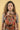 Parent wearing the Almitra Tattva Jataka Tales Kalamkari baby carrier in a front-carry position, featuring bold handcrafted-inspired Indian folk art prints in earthy red and mustard tones. Ergonomic soft structured baby carrier designed for newborns, infants, and toddlers with adjustable padded straps for inclusive, comfortable babywearing.