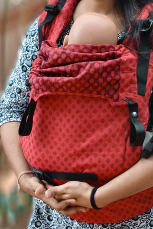 Front view of Almitra Tattva ergonomic baby carrier in bold red print with secure buckles and soft padded support, designed for mindful and inclusive babywearing.