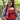 Smiling mother wearing Almitra Tattva red ergonomic baby carrier outdoors, carrying baby safely in a sustainable cotton babywearing carrier with adjustable straps and inclusive comfort design.