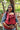 Smiling mother wearing Almitra Tattva red ergonomic baby carrier outdoors, carrying baby safely in a sustainable cotton babywearing carrier with adjustable straps and inclusive comfort design.