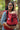 Mother smiling while carrying baby in Almitra Tattva ergonomic red baby carrier featuring soft woven fabric, adjustable straps, and inclusive eco-conscious babywearing support in a natural outdoor setting.