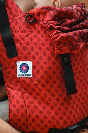 Close-up of Almitra Tattva red printed baby carrier featuring breathable fabric, ergonomic structure, adjustable black straps, and soft support for comfortable babywearing.