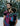 A bearded father wearing a toddler in an Almitra Tattva Pema Wrap Converted Ring Sling from the Kullu Collection. The sling features vibrant pink, turquoise, and black geometric handwoven patterns with a pink aluminum ring. The setting is a snowy winter landscape, emphasizing the bold, inclusive style of the brand.