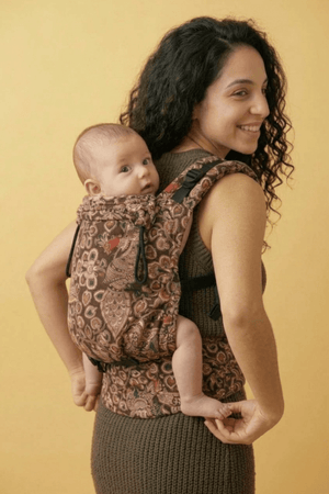 Back view of mother wearing Almitra Tattva paisley patterned ergonomic baby carrier with baby in secure back carry position, showcasing adjustable padded straps, inclusive fit, artisan-inspired print, and comfortable hands-free babywearing support.