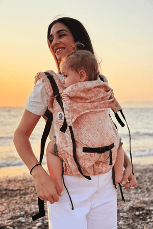 "Mother carrying her baby in a premium ergonomic soft structured baby carrier at the beach during sunset. Adjustable front baby carrier with ergonomic hip support, breathable fabric, and comfortable hands-free babywearing for newborns, infants, and toddlers."
