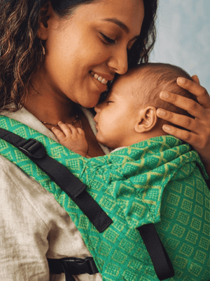 Intimate close-up of an infant asleep against their mother's chest inside the green handloom Mangalgiri cotton carrier panel.