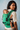 Over-the-shoulder view of a woman carrying her baby on her back in the green geometric woven Almitra Tattva baby carrier.