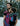 A bearded father wearing a toddler in an Almitra Tattva Pema Wrap Converted Ring Sling from the Kullu Collection. The sling features vibrant pink, turquoise, and black geometric handwoven patterns with a pink aluminum ring. The setting is a snowy winter landscape, emphasizing the bold, inclusive style of the brand.