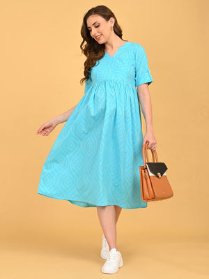 Aquamarine Affair Maternity and Nursing Dress in aquamarine blue with geometric print, V-neck and short sleeves, styled with white sneakers and a tan handbag.