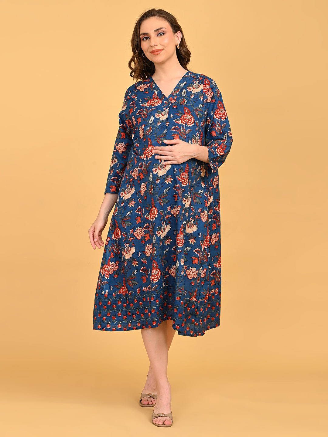 Pregnant model wearing blue floral maternity and nursing midi dress, holding orange leaves against beige background.
