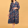 Pregnant model wearing blue floral maternity and nursing midi dress, holding orange leaves against beige background.