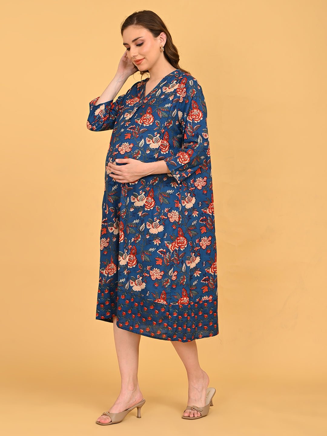 Close-up of blue floral maternity dress with V-neckline, model holding orange leaves near baby bump.