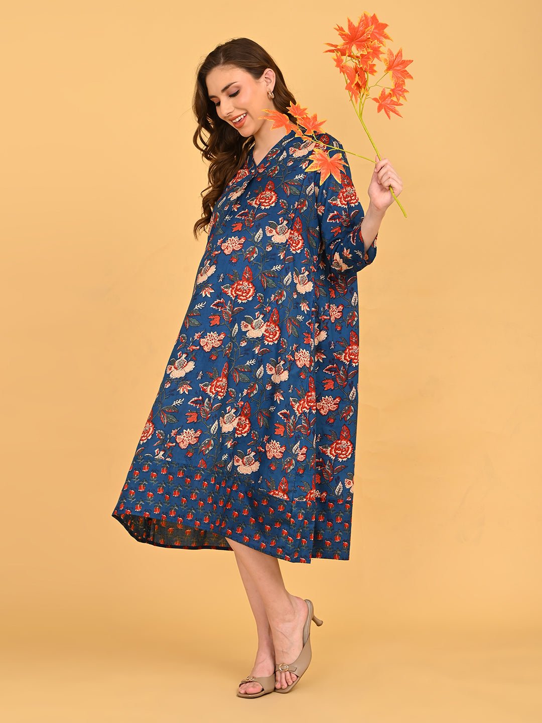 Pregnant model posing in blue floral maternity and nursing dress while holding decorative orange leaves.