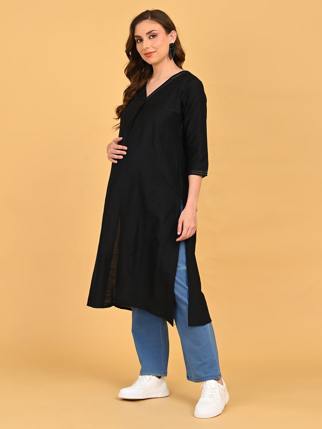 Pregnant model wearing black embroidered maternity silk kurta paired with blue straight-fit pants and white sneakers.