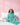 Child wearing teal pajamas with unicorn prints, sitting on a bed against a pink wall