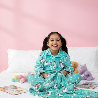 Child wearing teal pajamas with unicorn prints, sitting on a bed against a pink wall