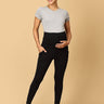 A pregnant woman wearing black maternity leggings with a wide, belly support waistband, paired with a short grey top.