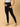 A pregnant woman wearing black maternity leggings with a wide, belly support waistband, paired with a short grey top.