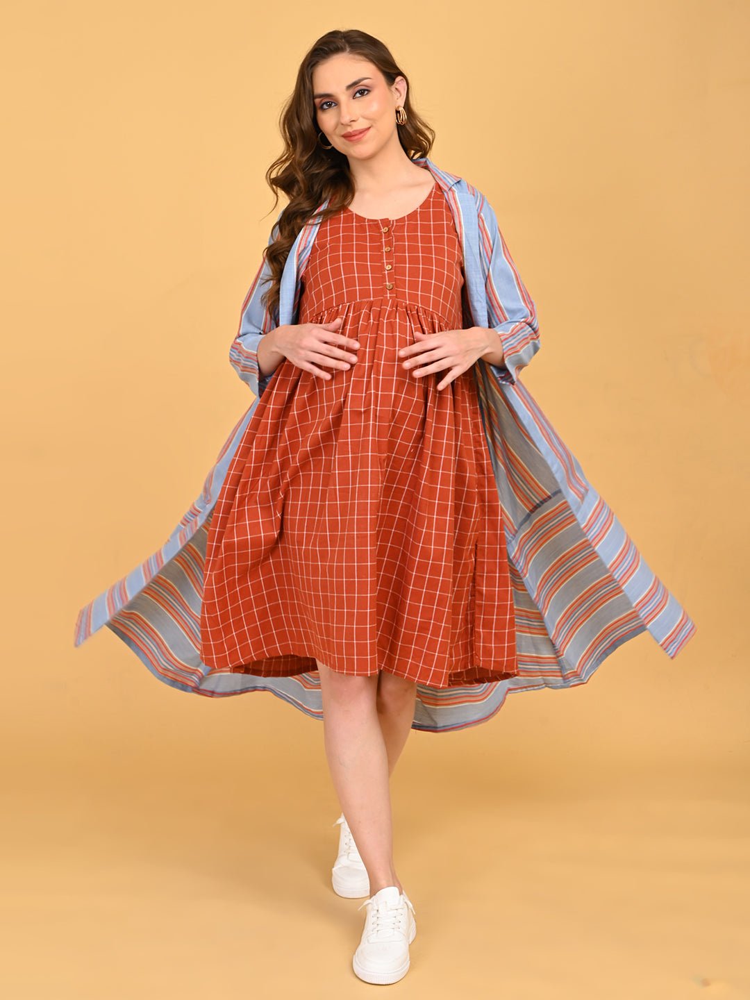 Pregnant model wearing Copper Daybreak maternity check dress with blue striped long shacket, walking in white sneakers.