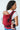 A baby looking over their mother's shoulder while seated safely in the red Almitra Tattva Aruna handwoven cotton baby carrier.