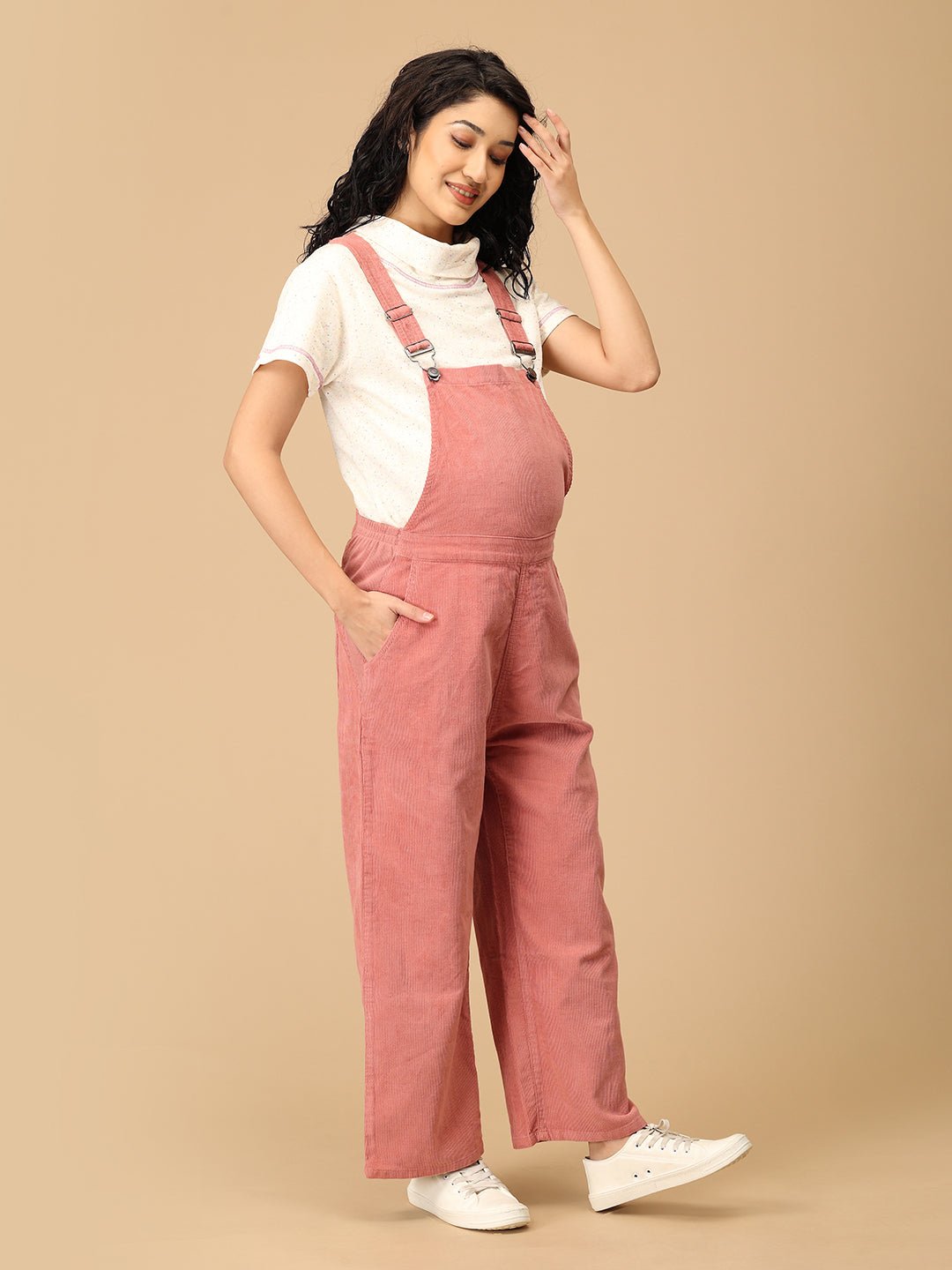 Relaxed pose wearing The Mom Store dusky rose corduroy maternity dungaree with pockets.