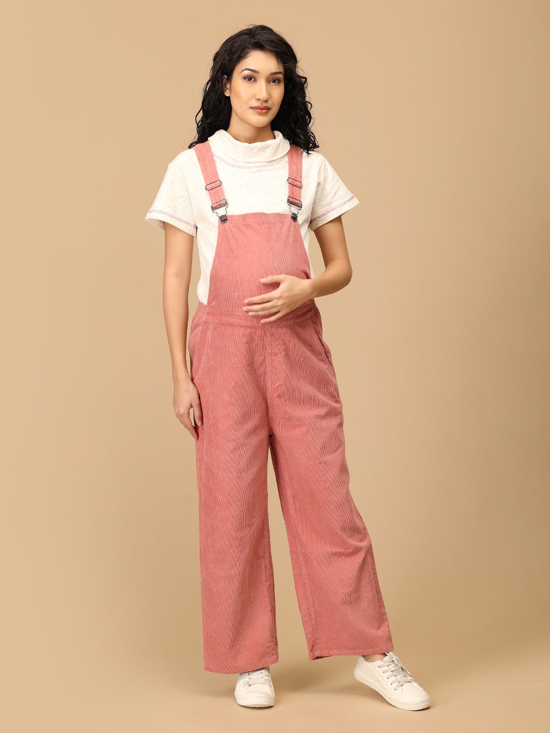 Pregnant woman smiling in The Mom Store dusky rose corduroy maternity dungaree front pose.