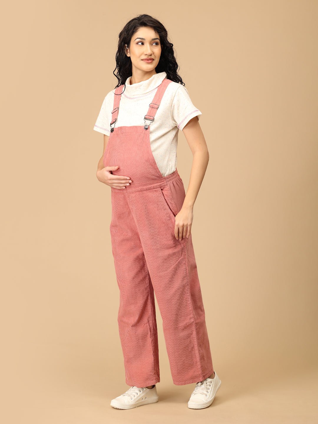 Side pose of pregnant woman in The Mom Store dusky rose corduroy maternity dungaree.