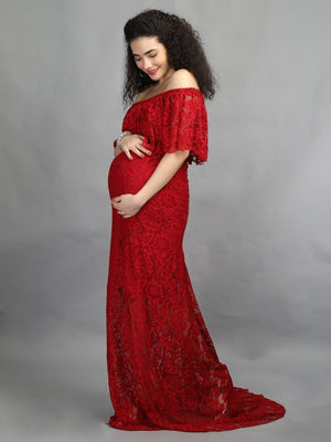 Playful side pose of a pregnant lady wearing wine coloured, off-shoulder maternity maxi dress from The Mom Store, touching her bump.