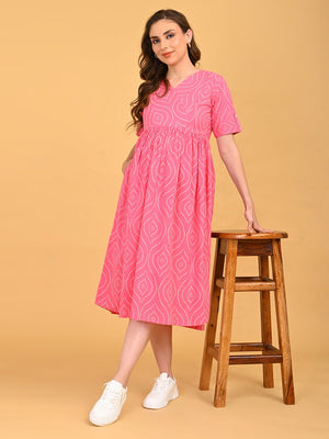 Flamingo Flirt Maternity and Nursing Dress featuring empire waist and flowy midi silhouette, styled with white sneakers and a wooden stool.