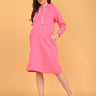 Angled side view of fuchsia maternity hoodie dress with hands on bump and pocket detail.