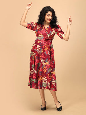 Woman posing with raised arms in a garnet red floral maternity and nursing wrap dress featuring a vibrant leaf print.