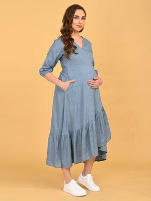 Portrait of a lady wearing Grey Escape Maternity Wrap Dress, standing against orange background with her hands inside the pockets