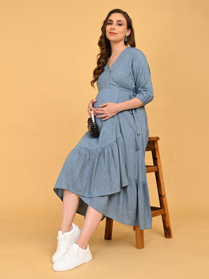 A pregnant woman sitting on a wooden chair wearing Grey Escape Maternity Wrap Dress and white sneakers