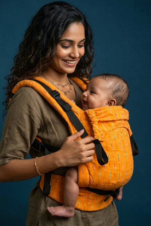 Close-up view of the mother holding the padded black shoulder strap adjustment on the orange and yellow Ikkat baby carrier.