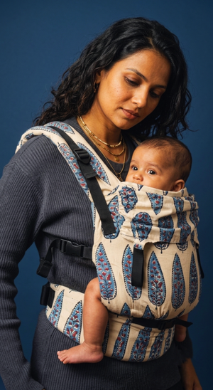 Front-side view of an infant resting securely in the Almitra Tattva Ajrakh baby carrier, highlighting the ergonomic inward-facing position and the wide, patterned waistbelt.