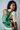 Over-the-shoulder view of a woman carrying her baby on her back in the green geometric woven Almitra Tattva baby carrier.