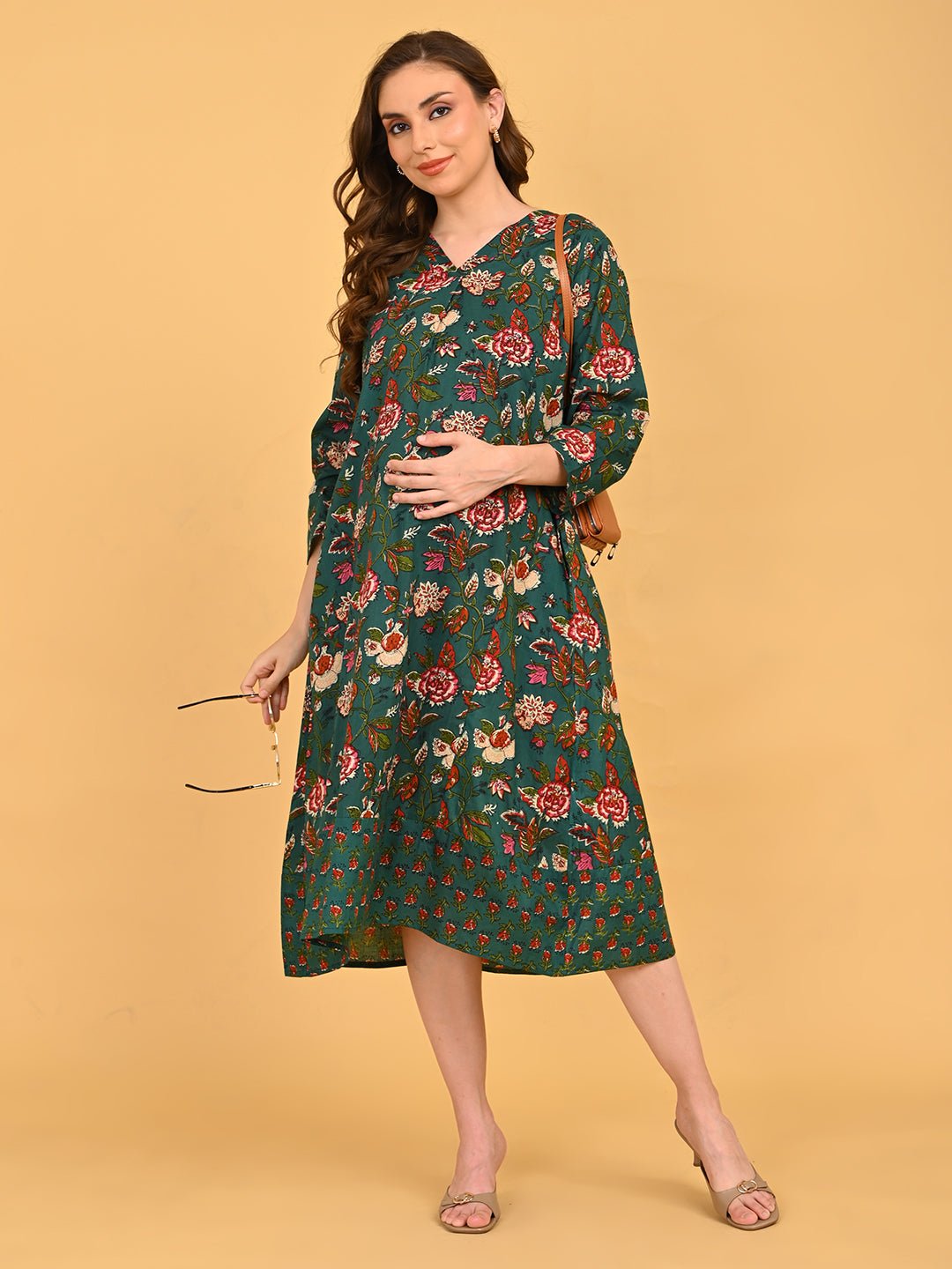 Model walking in green floral maternity and nursing midi dress styled with beige heels.